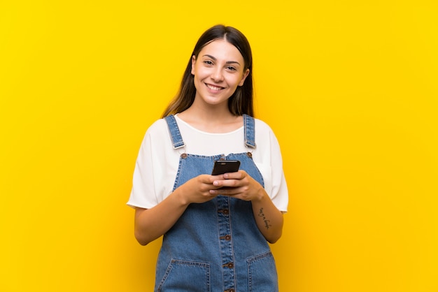 Jeune femme en salopette envoyant un message avec le portable