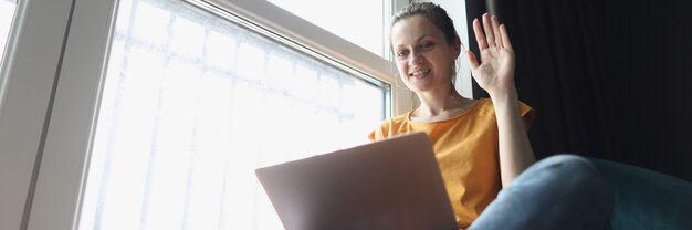 Jeune femme saluant l'ordinateur portable alors qu'il était assis sur le rebord de la fenêtre