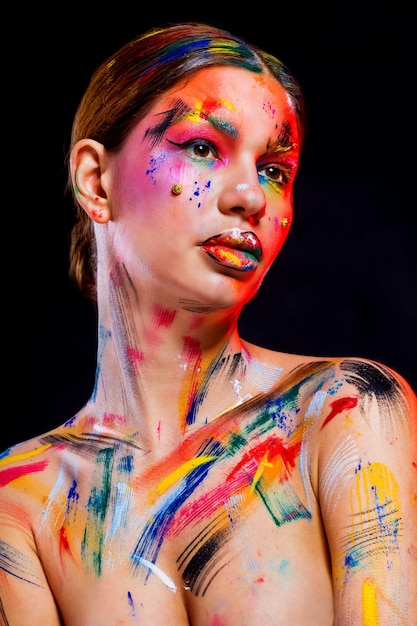 Une jeune femme sans chemise avec des peintures colorées sur son corps sur un fond noir