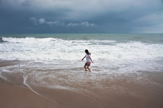 Jeune femme sautant dans la mousse des vagues de la mer pendant la tempête contre le ciel pluvieux Koh Samui Thaïlande