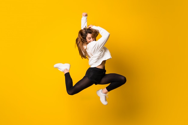 Jeune femme sautant par-dessus un mur jaune isolé