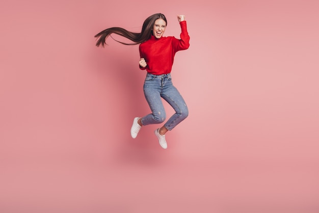Une jeune femme sautant en plein air célèbre sa victoire sur fond rose