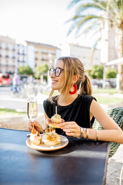 Jeune femme savourant un apéritif savoureux avec des pinchos, une collation espagnole traditionnelle, avec un verre de vin assis à l'extérieur au bar de la ville de Valence