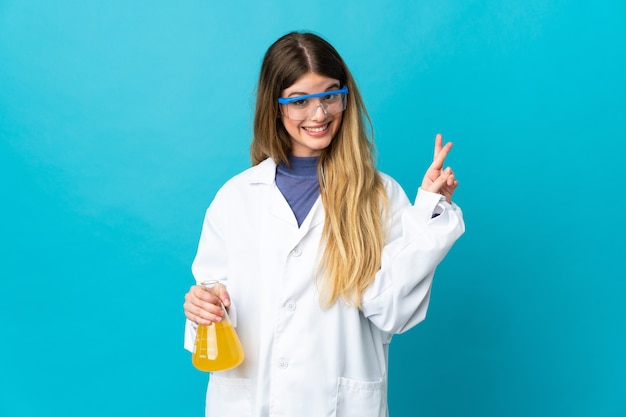 Jeune femme scientifique blonde isolée sur mur bleu avec les doigts qui se croisent et souhaitant le meilleur