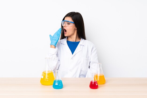 Jeune femme scientifique dans une table bâillant et couvrant la bouche grande ouverte avec la main