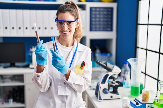 Jeune femme scientifique souriant confiant tenant des tubes à essai au laboratoire