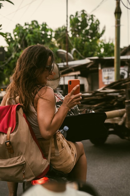 Une jeune femme en scooter voyage prend des photos au téléphone.