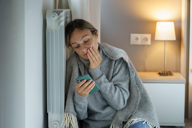 Une Jeune Femme Se Blottissant Contre Une Batterie Froide Perd Sa Motivation Et Son Sens De La Vie Et Fait Défiler Son Téléphone