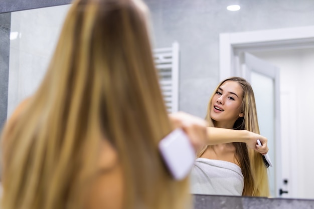 Jeune femme se brosser les cheveux sains devant un miroir dans la salle de bain