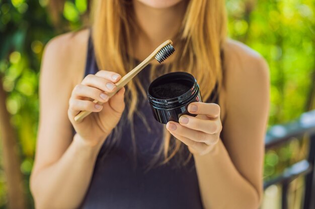 Jeune femme se brosser les dents à l'aide de poudre de charbon actif pour se brosser et blanchir les dents Brosse écologique en bambou