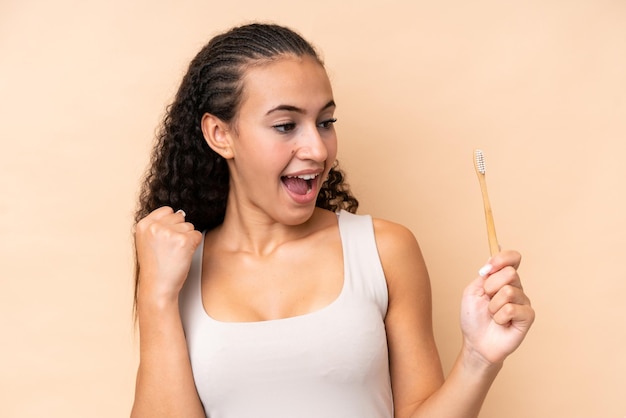 Jeune femme se brosser les dents isolé sur fond beige célébrant une victoire