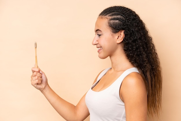 Jeune femme se brosser les dents isolé sur fond beige avec une expression heureuse