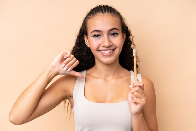 Jeune femme se brosser les dents isolée sur fond beige fière et satisfaite