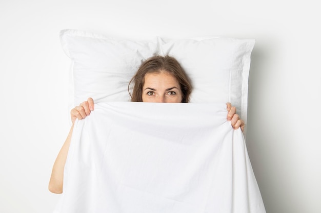 Jeune femme se couvrant d'un drap blanc en position allongée sur le lit Vue de dessus mise à plat