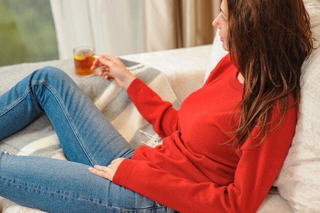 Jeune femme se détendre sur le canapé tenant une tasse avec du thé au citron femme rêvant dans le salon allongé sur le canapé