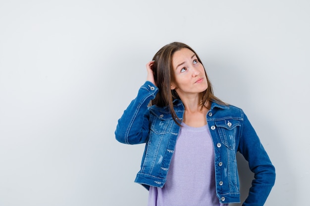 Jeune femme se grattant la tête, levant les yeux en t-shirt, veste et l'air réfléchi, vue de face.