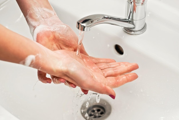 Jeune femme se lavant les mains sous le robinet d'eau avec du savon. Détail sur le liquide sur la peau. Mousse de savon sur le poignet, concept d'hygiène personnelle.