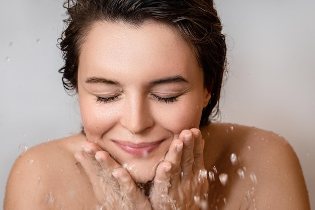 Jeune femme se lavant le visage avec de l'eau propre