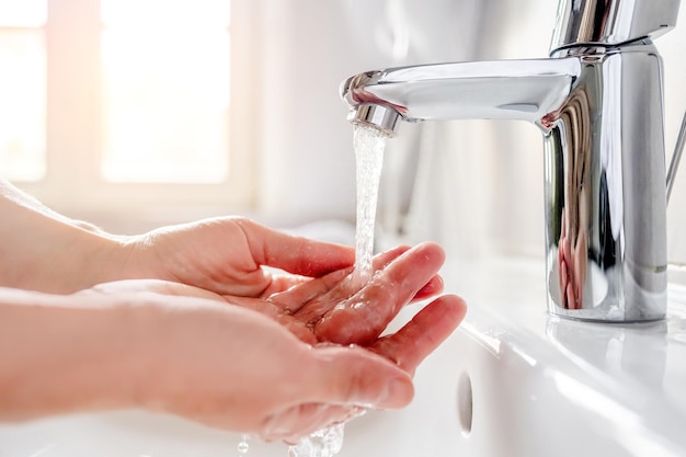 Une jeune femme se lave les mains avec du savon sur le lavabo dans la salle de bain en gros plan