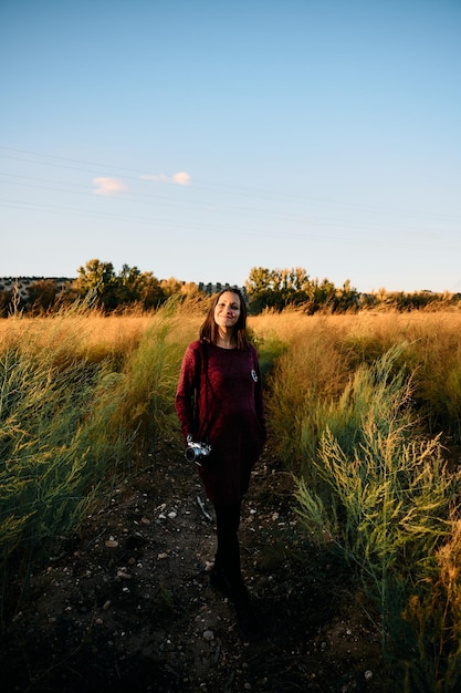 Une jeune femme se promenant dans la campagne avec son appareil photo vintage au coucher du soleil