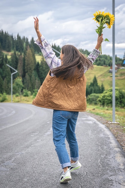 Une jeune femme se promène dans les montagnes avec un bouquet de tournesols