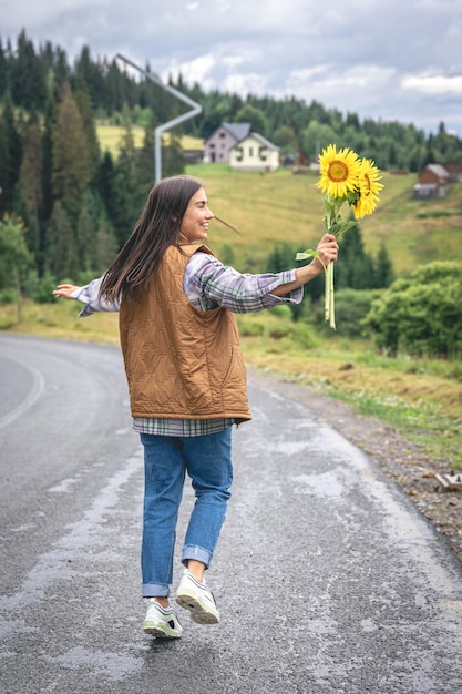 Une jeune femme se promène dans les montagnes avec un bouquet de tournesols