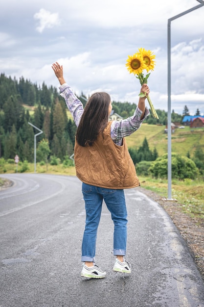 Une jeune femme se promène dans les montagnes avec un bouquet de tournesols