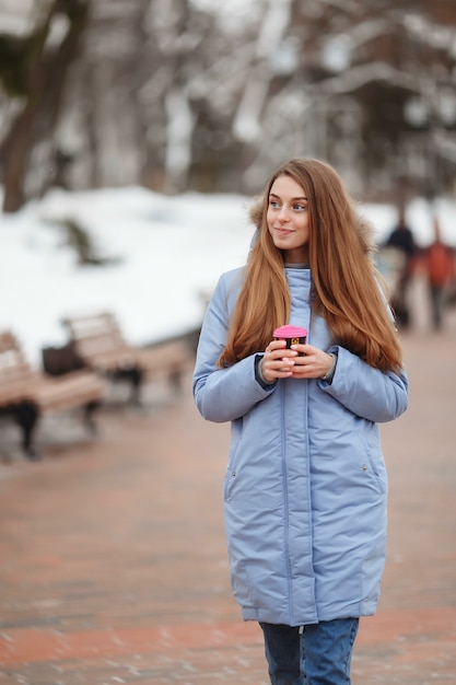 Jeune femme se promène dans un parc d'hiver avec du café.