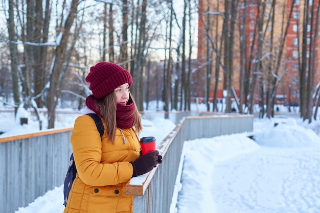 Une jeune femme se promène dans un parc d'hiver avec une tasse de café dans les mains