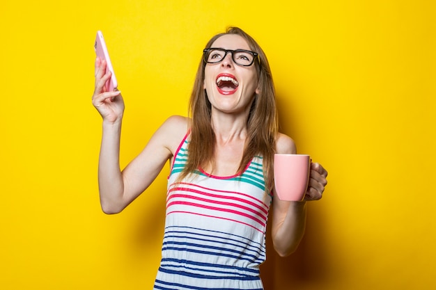 Jeune femme se réjouit avec une tasse de café et avec un téléphone