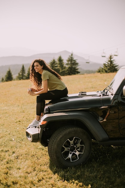 Jeune femme se reposant sur un capot de véhicule tout-terrain à la campagne