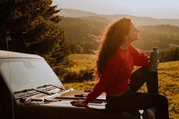 Jeune femme se reposant sur un capot de véhicule tout-terrain à la campagne