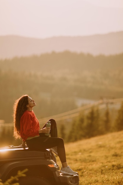 Jeune femme se reposant sur un capot de véhicule tout-terrain à la campagne