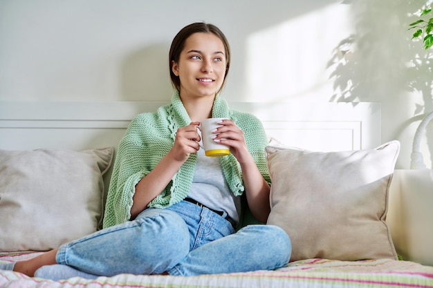 Jeune femme se reposant avec une tasse de thé chaud assis sur un canapé à la maison