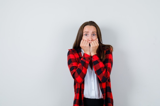 Jeune femme se rongeant les ongles avec émotion dans des vêtements décontractés et l'air anxieux, vue de face.