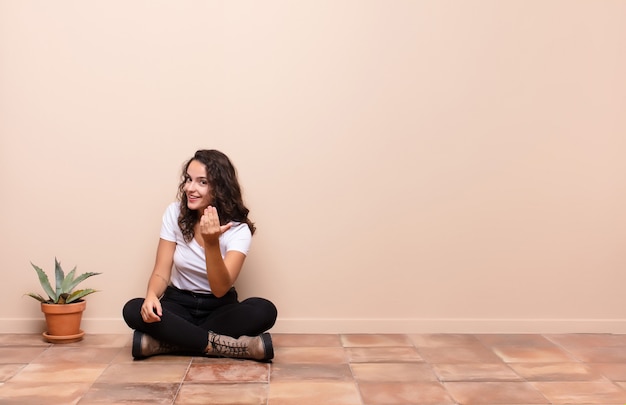 Jeune femme se sentant heureuse, réussie et confiante, faisant face à un défi et disant: amenez-le! ou vous accueillir assis sur une terrasse au sol