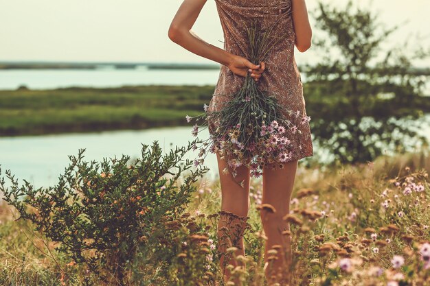 La jeune femme se tient en arrière et tient un bouquet de fleurs dans la nature. Fleurs d'automne des steppes..