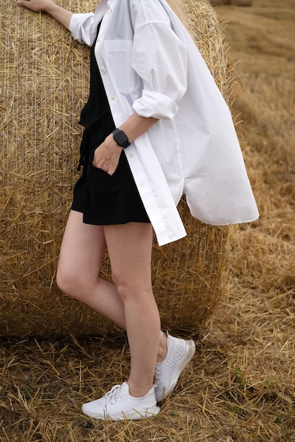 Une jeune femme se tient à côté d'une pile de paille roulée dans la saison des récoltes d'été sur le terrain