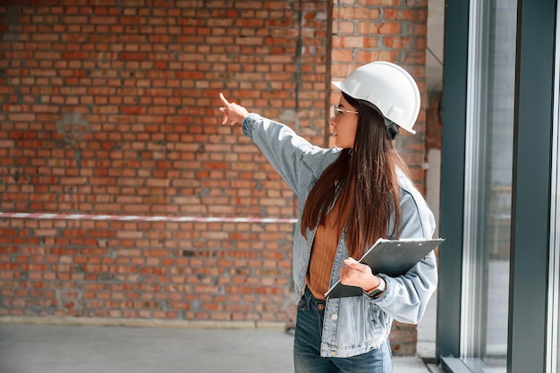 Photo la jeune femme se tient dans le bâtiment inachevé sur le chantier de construction et travaille sur un projet