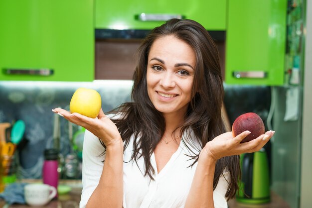 Jeune femme se tient dans la cuisine tenant des fruits dans ses mains fille de race blanche dans une cuisine moderne détient g...