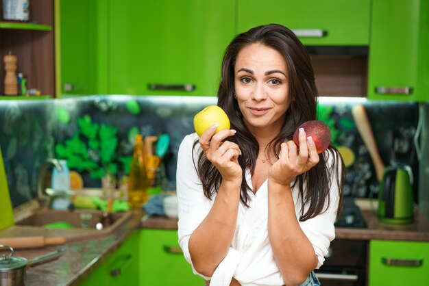 Jeune femme se tient dans la cuisine tenant des fruits dans ses mains