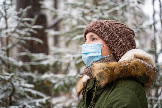 Une jeune femme se tient dans une forêt d'hiver dans laquelle il neige et regarde comment la neige tombe