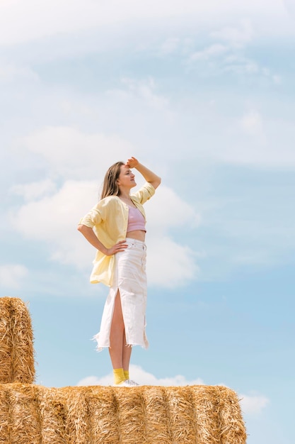 Jeune femme se tient sur une haute botte de foin et regarde au loin Vacances à la campagne Récolte du foin pour l'hiver