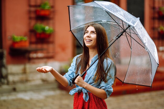 Une jeune femme se tient avec un parapluie à la main dans la rue et regarde la caméra