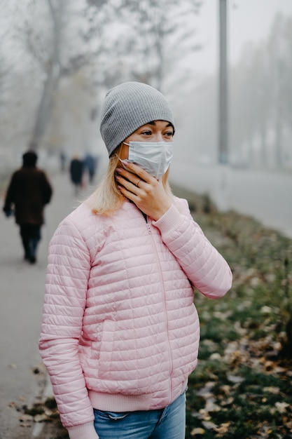 Une jeune femme se tient près de la route dans un masque médical à l'automne.