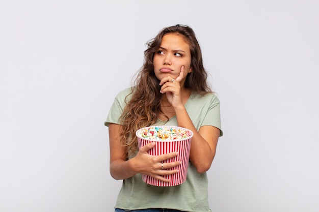 Jeune femme avec un seau pop conrs penser, se sentir douteux et confus, avec différentes options, se demandant quelle décision prendre