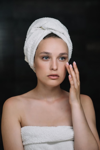 Photo une jeune femme séduisante applique une crème pour le visage dans un miroir, une belle femme en bonne santé enveloppée dans des serviettes met une crème de jour nourrissante et hydratante sur une peau douce et hydratée