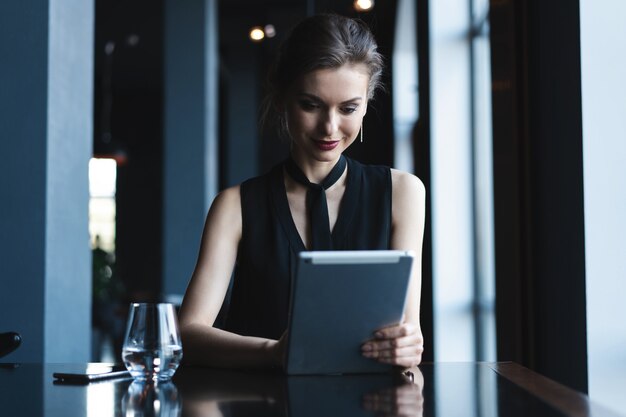 Jeune femme séduisante assise dans un café pendant son temps libre et travaillant sur une tablette. Heureuse femme se reposer au café. Mode de vie.