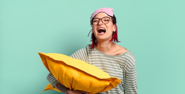 Jeune femme séduisante aux cheveux roux criant agressivement, l'air très en colère, frustrée, indignée ou agacée, criant non et portant un pyjama.