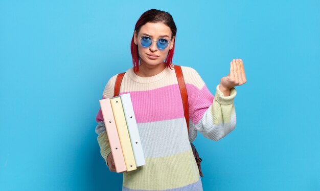 Jeune femme séduisante aux cheveux roux faisant capice ou geste d'argent, vous disant de payer vos dettes!. concept d'étudiant universitaire